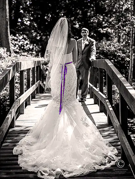 back of beautiful Tunbridge Wells wedding dressed with purple lace tie presented as bride stands on lilly pond bridge at Salomons Estate