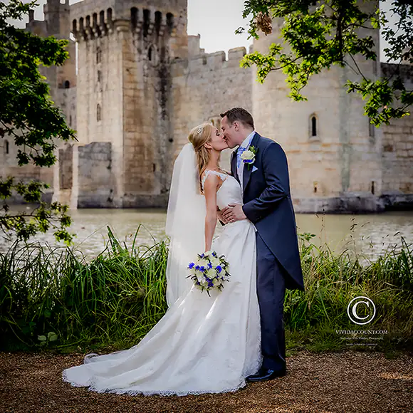 Groom embraces and kisses his newly wed bride during their wedding reception in front of Bodiam Castle near Tunbridge Wells, Kent