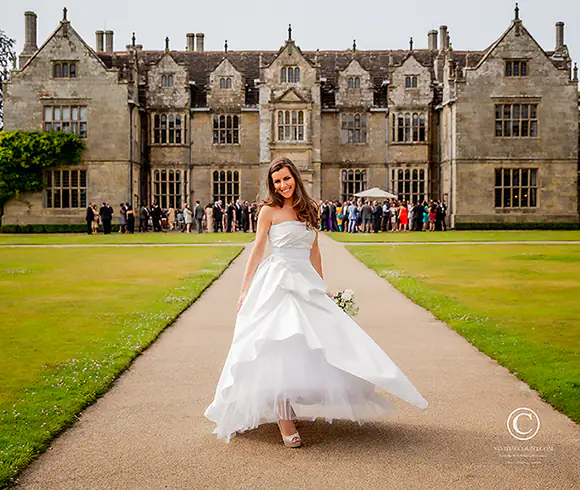 Bride stands in front of Wakehurst place and her wedding guests for a very informal portrait