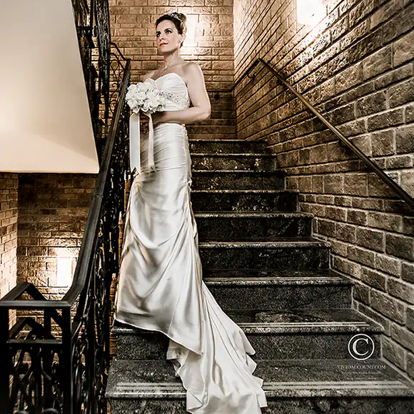 Bride posing in white Tunbridge Wells wedding gown holding bouquet of white roses on the granite staircase at her wedding venue