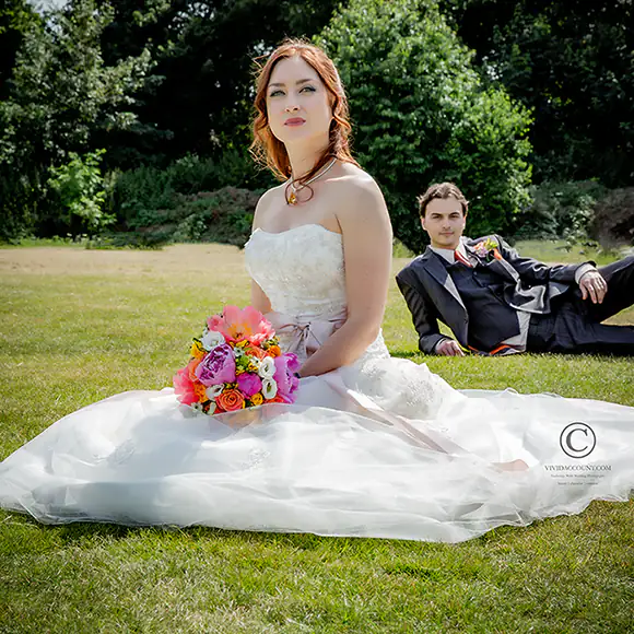 Bride and groom seated on the ground with a very colourful wedding bouquet taking prominence
