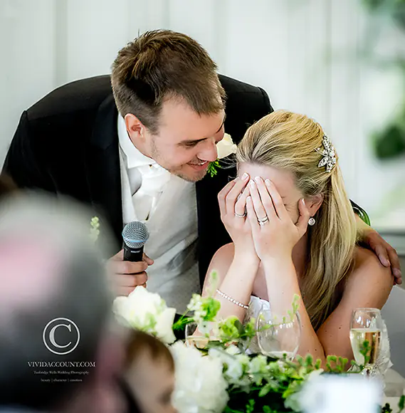 Bride buries her head in her hands with pretend embarrassment during her husband's wedding speech