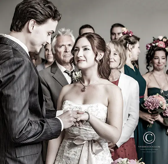 Bride and groom exchange wedding rings in front of emotional wedding guests