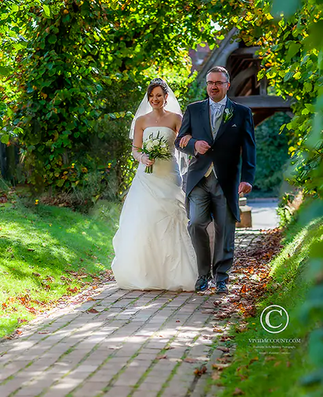father of bride escorts his daughter into church near Tunbridge Wells along a brick walkway surrounded by green to begin her church wedding service