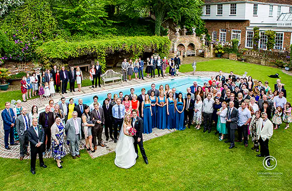 Bride, groom and all wedding guests arranged around the simming pool at Powdermills Hotel near Tunbridge Wells for a group wedding photo