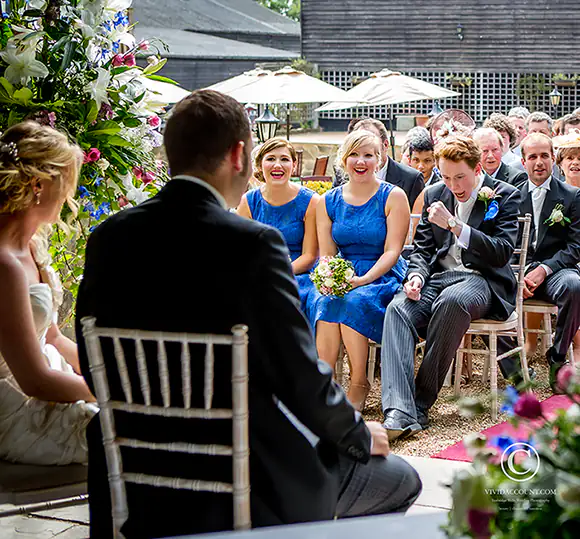 Wedding guests at Swallows Oast, Ticehurst near Tunbridge Wells react with smiles and cheers to the celebrant during an outdoors summer wedding ceremony