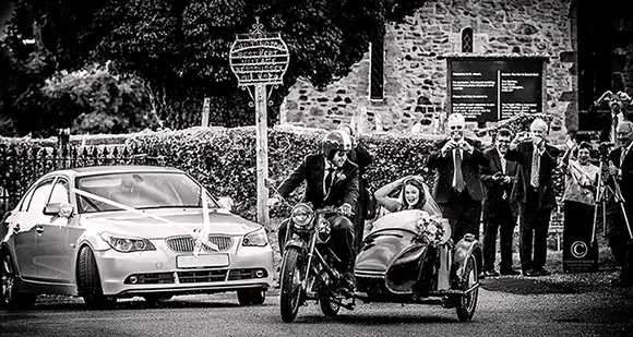 bride driven away from wedding ceremony in a motorcycle sidecar by her new husband on a classic motorcycle