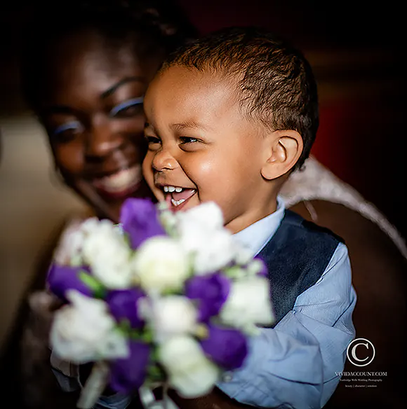 Pageboy with a big smile as he holds the bride's  purple and white Tunbridge Wells wedding bouquet