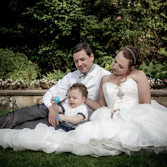 newly married husband and wife sit with their son in the grounds of their home in Southborough, Tunbridge Wells for a wedding day family portrait