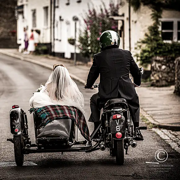 Groom on a classic motorbike driving his newly married wife in motorcycle sidecar from church to their Tunbridge Wells wedding reception venue