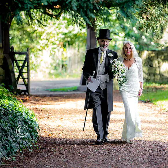 Groom with silver cane walks with his bride along a gravel pathway in the Tunbridge Wells countryside