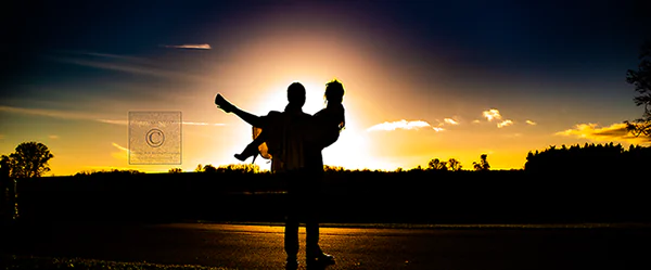 Groom cradles bride in his arms as they are both silhoutted in a golden Tunbridge Wells, Kent sunset on their wedding day