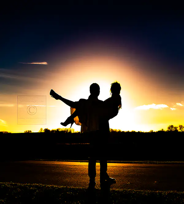 Groom cradles bride in his arms as they are both silhoutted in a golden Tunbridge Wells, Kent sunset on their wedding day